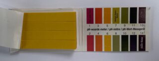 Gele papiertjes met ernaast gekleurde strepen die een pH-waarde uitdrukken